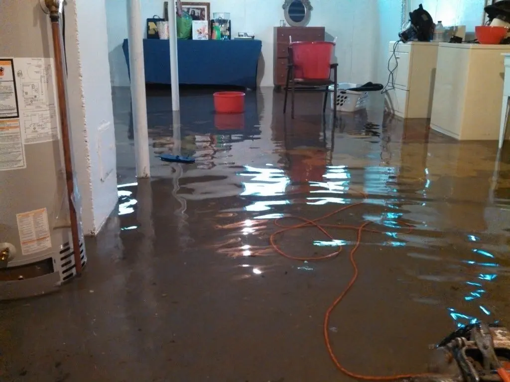 Flooded basement with standing water on the floor next to a water heater