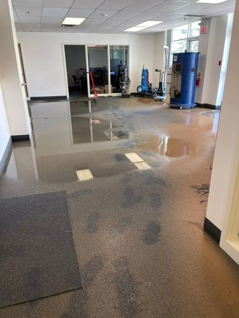 Standing water across a flooded office floor, with water extraction equipment set up in the background