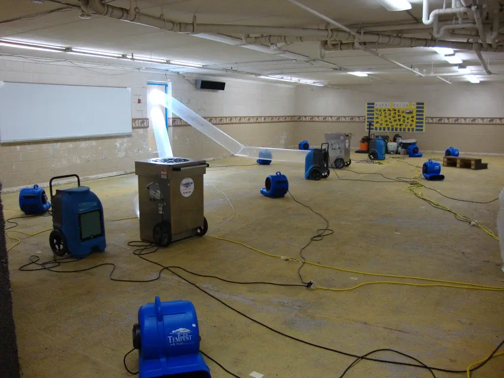 Air movers and dehumidifiers drying a large commercial room after water damage