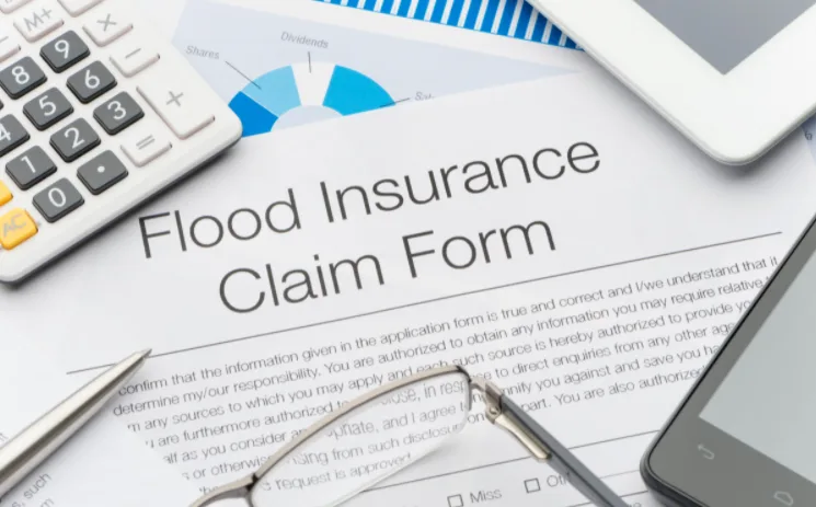 Flood insurance claim form on a desk next to a calculator, pen and glasses